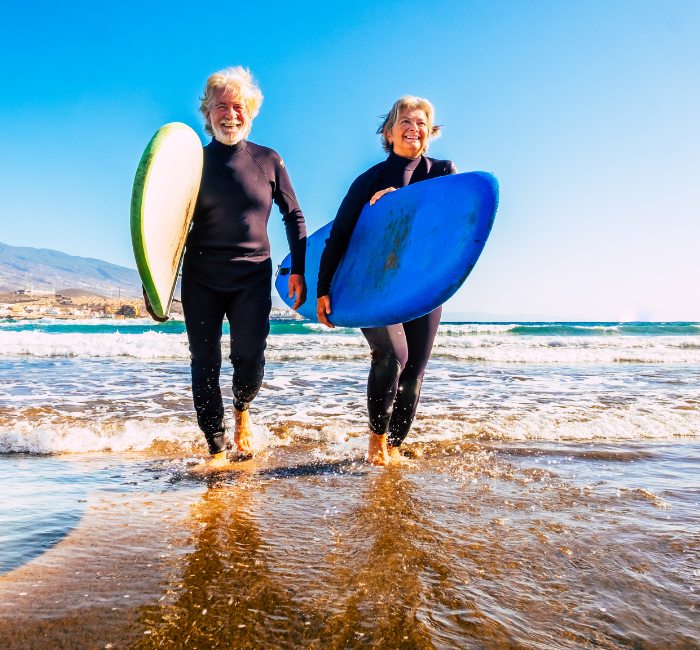 Fit, healthy older couple in wetsuits carrying surfboards in the shallow water of a sunny beach