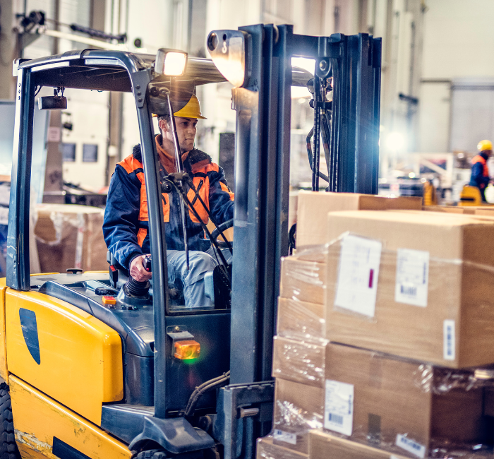 Forklift truck driver moving stack of heavy boxes wearing a high-vis jacket and hardhat