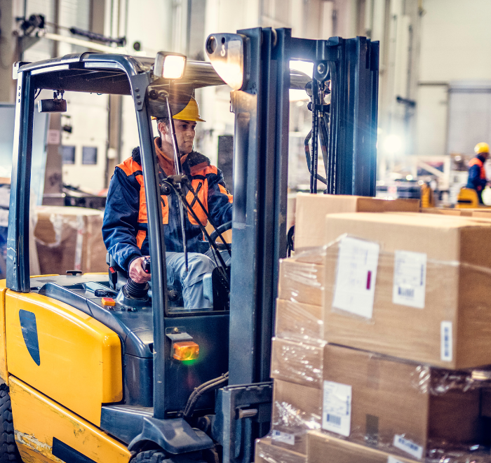 Forklift truck driver moving stack of heavy boxes wearing a high-vis jacket and hardhat