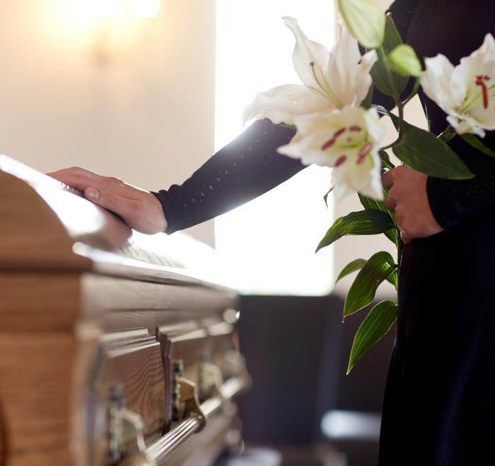 Mourning relative touching a wooden coffin at a funernal to pay respsects